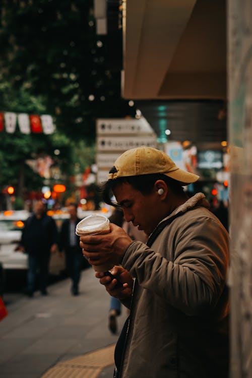 Man in Cap Standing with Cup on Sidewalk