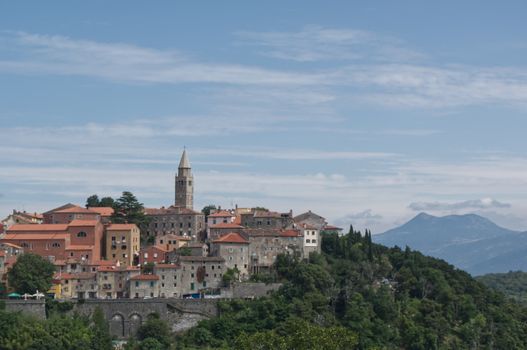 A picturesque historic town with colorful houses and a central tower set against a mountain backdrop.