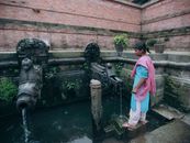 A woman stands by traditional stone water spouts in a historic courtyard.