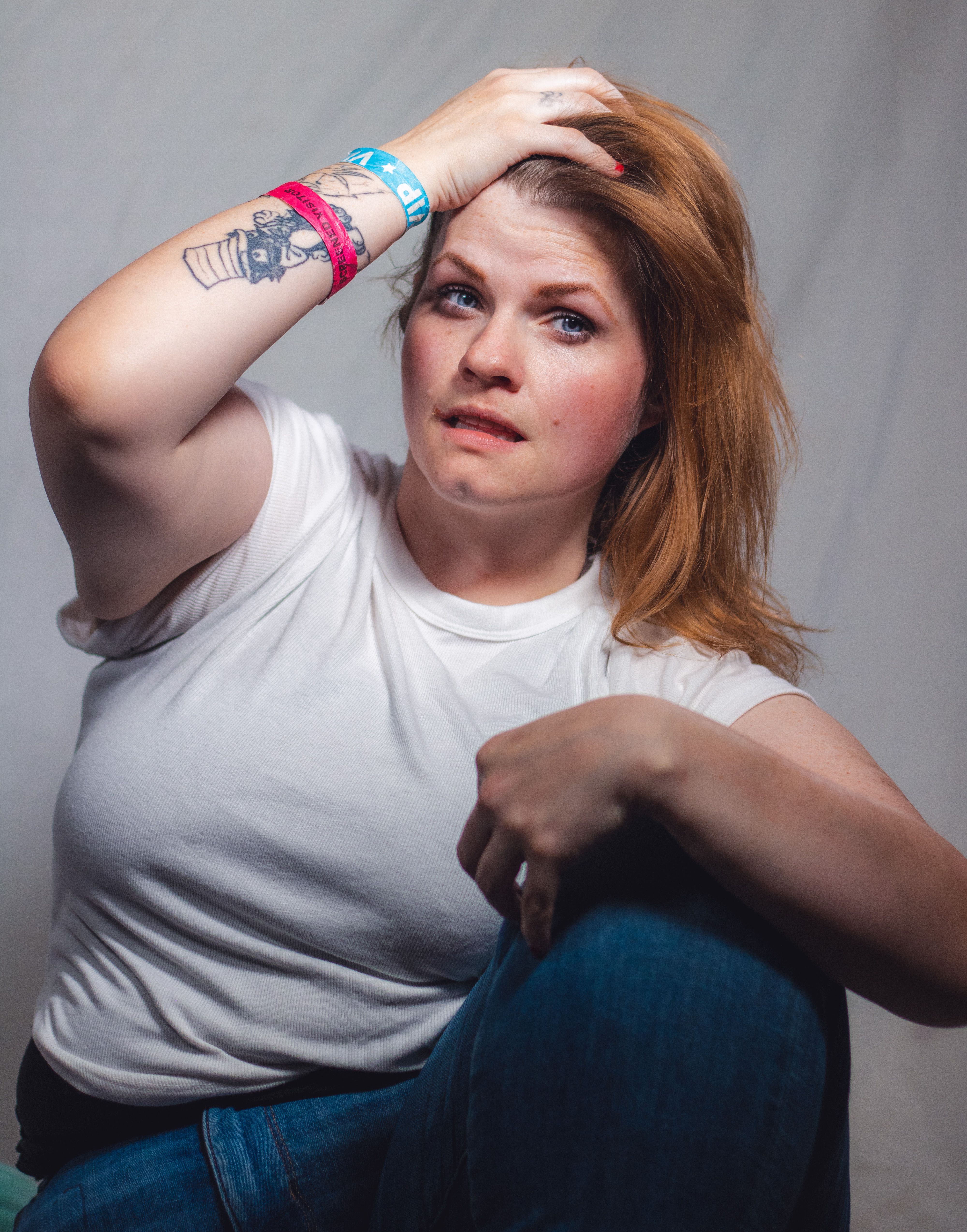 A woman with tattoos poses confidently in a studio, showcasing her unique style and personality.