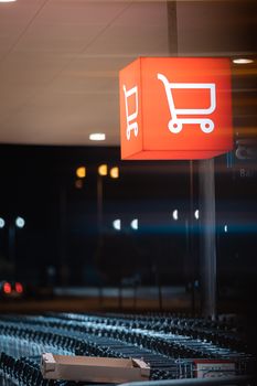 Vibrant shopping cart icon glowing above rows of carts at a supermarket at night.
