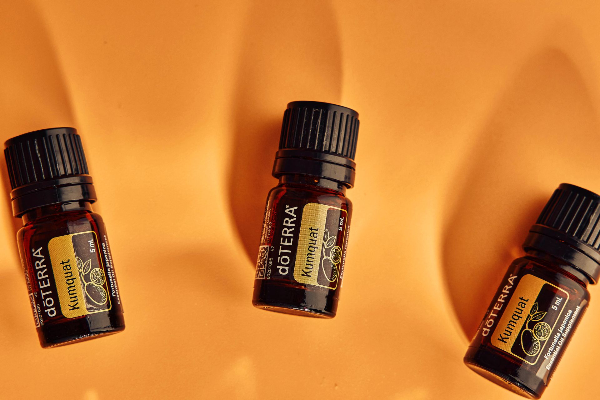 Flat lay of dÅTERRA kumquat essential oil bottles on an orange background.