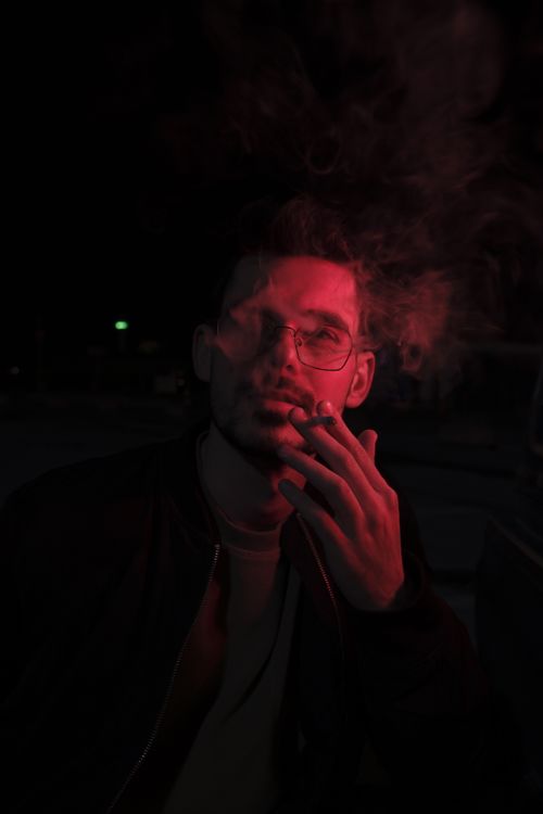 Free A dramatic portrait of a man smoking in moody red lighting, capturing a sense of mystery. Stock Photo