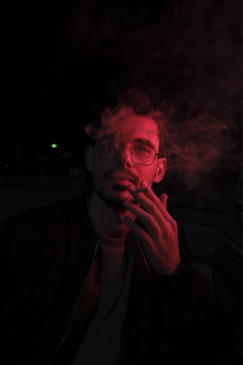 Free Artistic portrait of a man smoking under dim red lighting at night. Stock Photo