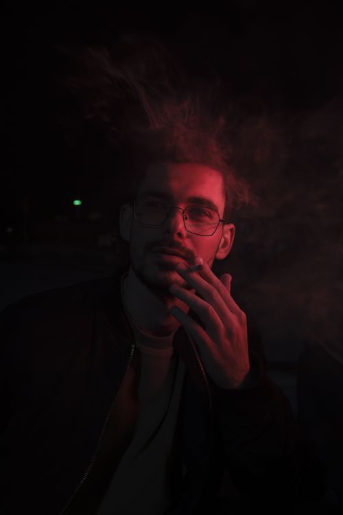 Free Artistic portrait of a man in red light with cigarette smoke, creating a mysterious mood. Stock Photo
