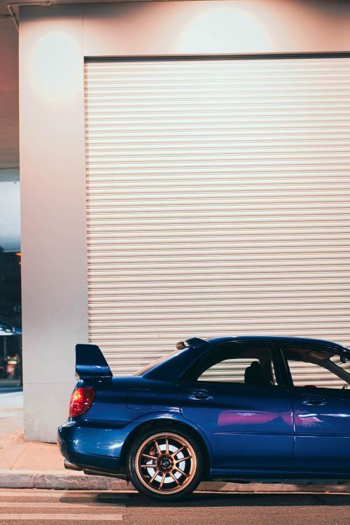 Free A striking blue sports car parked outdoors against an industrial wall at night. Stock Photo