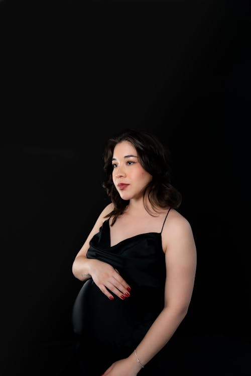 Studio Shoot of a Pregnant Woman Wearing a Black Dress against Black Background