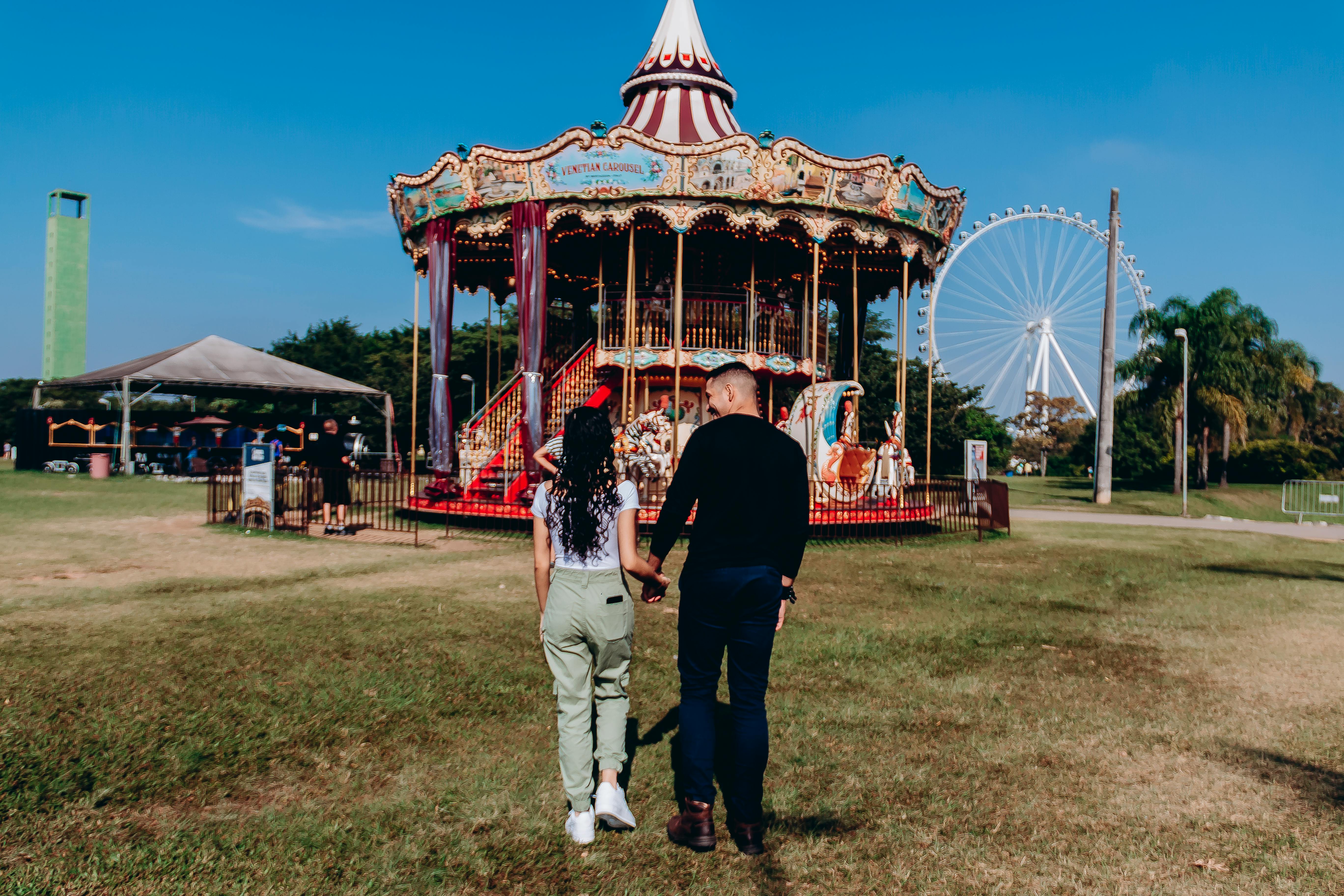 couple holding hands and walking near carousel in park in london