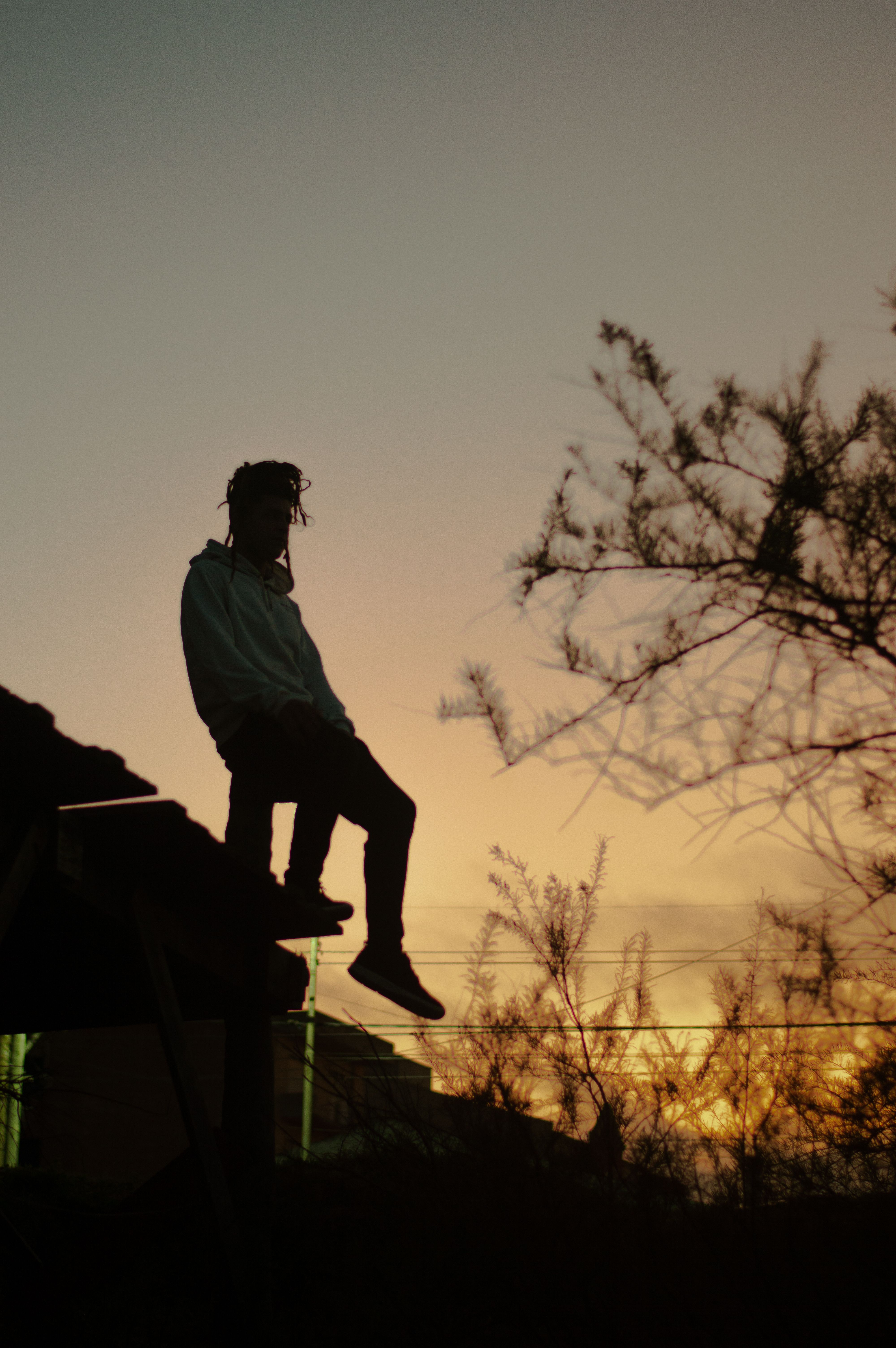 A silhouette of a person sitting on a rooftop against a vibrant sunset in Santa Teresita, Argentina.. pexels, silhouette, per