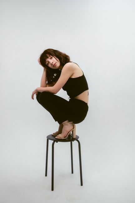 Elegant fashion model sitting on a stool wearing a stylish black outfit.