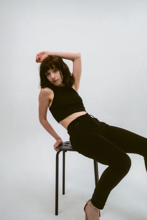 Free Stylish woman in black attire posing elegantly on a chair in a minimal setting. Stock Photo