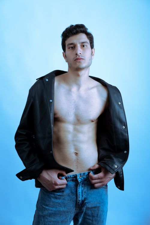 Free A confident young man posing in a black jacket against a blue background, embodying modern fashion. Stock Photo