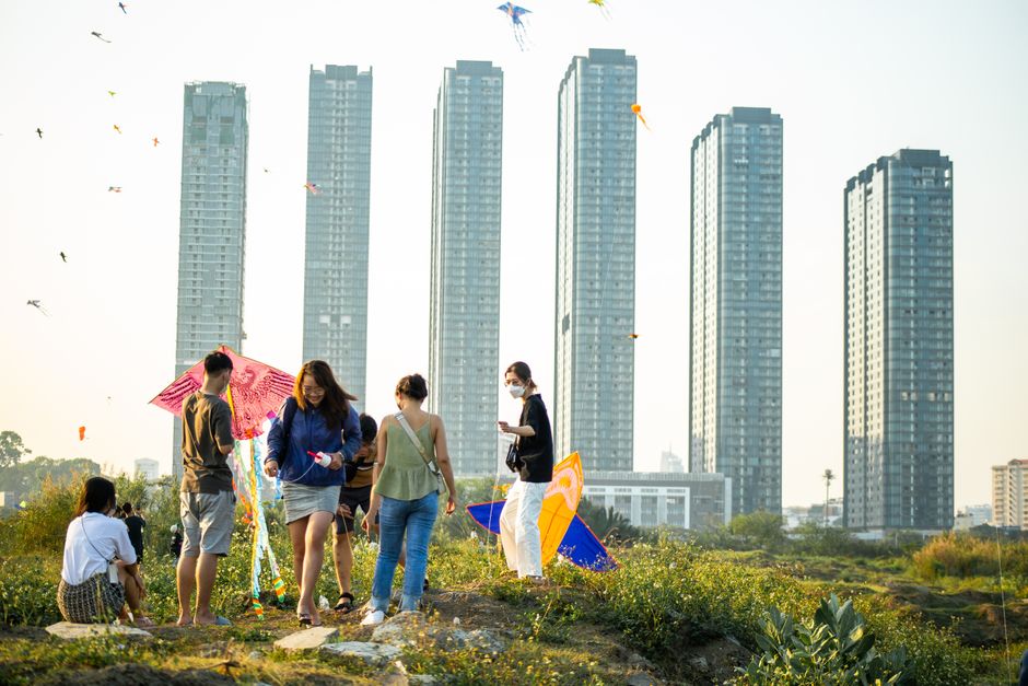 Group of adults enjoying kite flying near tall skyscrapers in Ho Chi Minh City under a clear day.