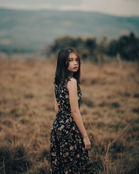 Elegant woman standing in a scenic grassland wearing a floral dress, captured in a portrait-style image.