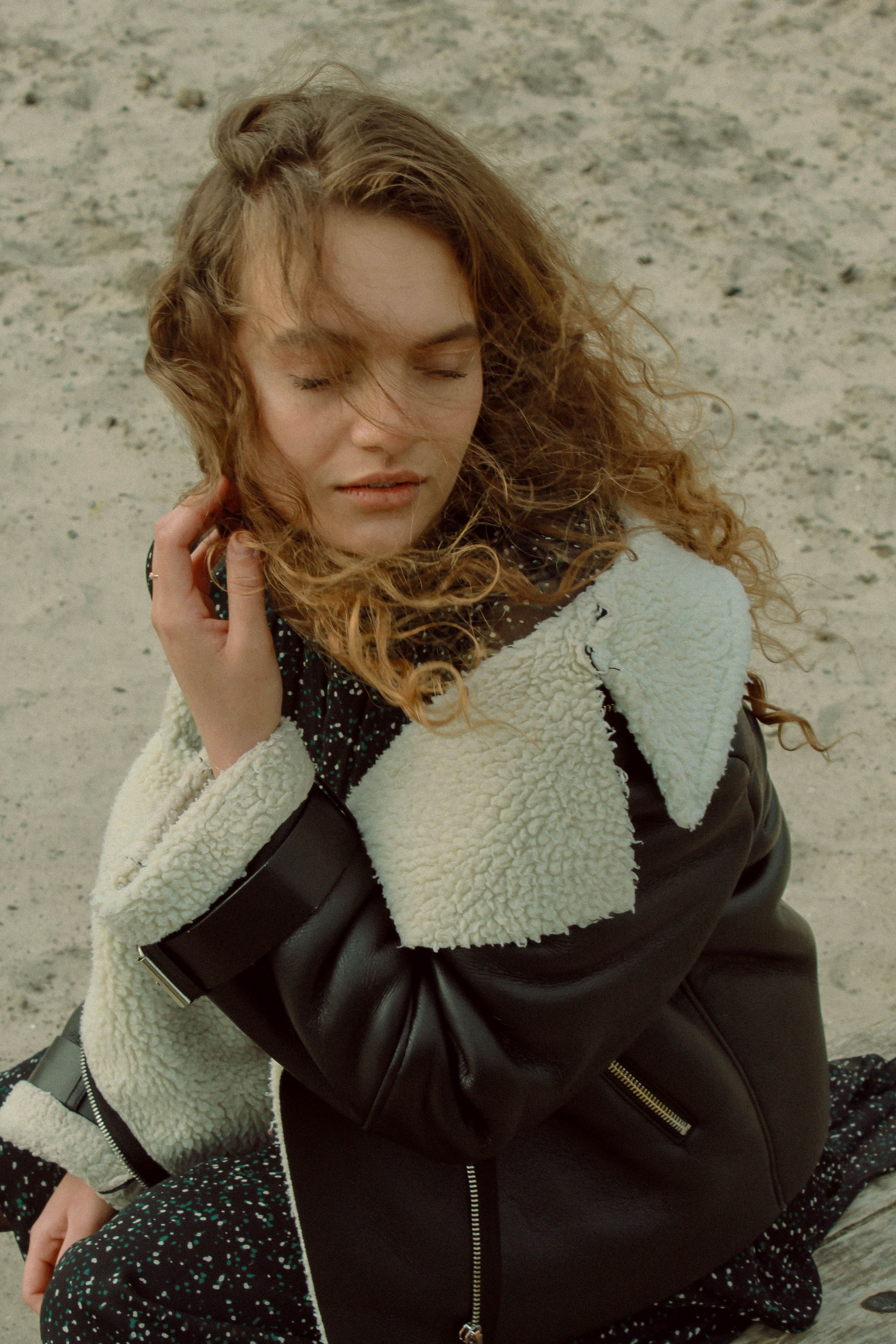 Stylish young woman with curly hair posing outdoors in a cozy jacket on a windy day.