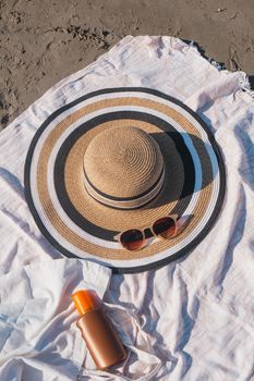 Close-up of beach essentials including sun hat, sunglasses, and sunscreen on blanket.