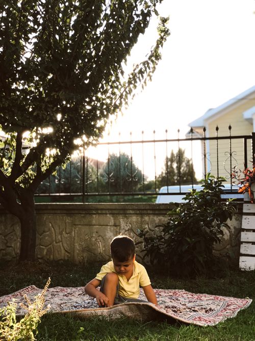 Free Boy with short hair sitting on a blanket in a garden, shaded by a tree, during the day. Stock Photo