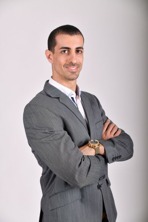 Free Businessman in a grey suit posing confidently with arms crossed against a neutral background. Stock Photo