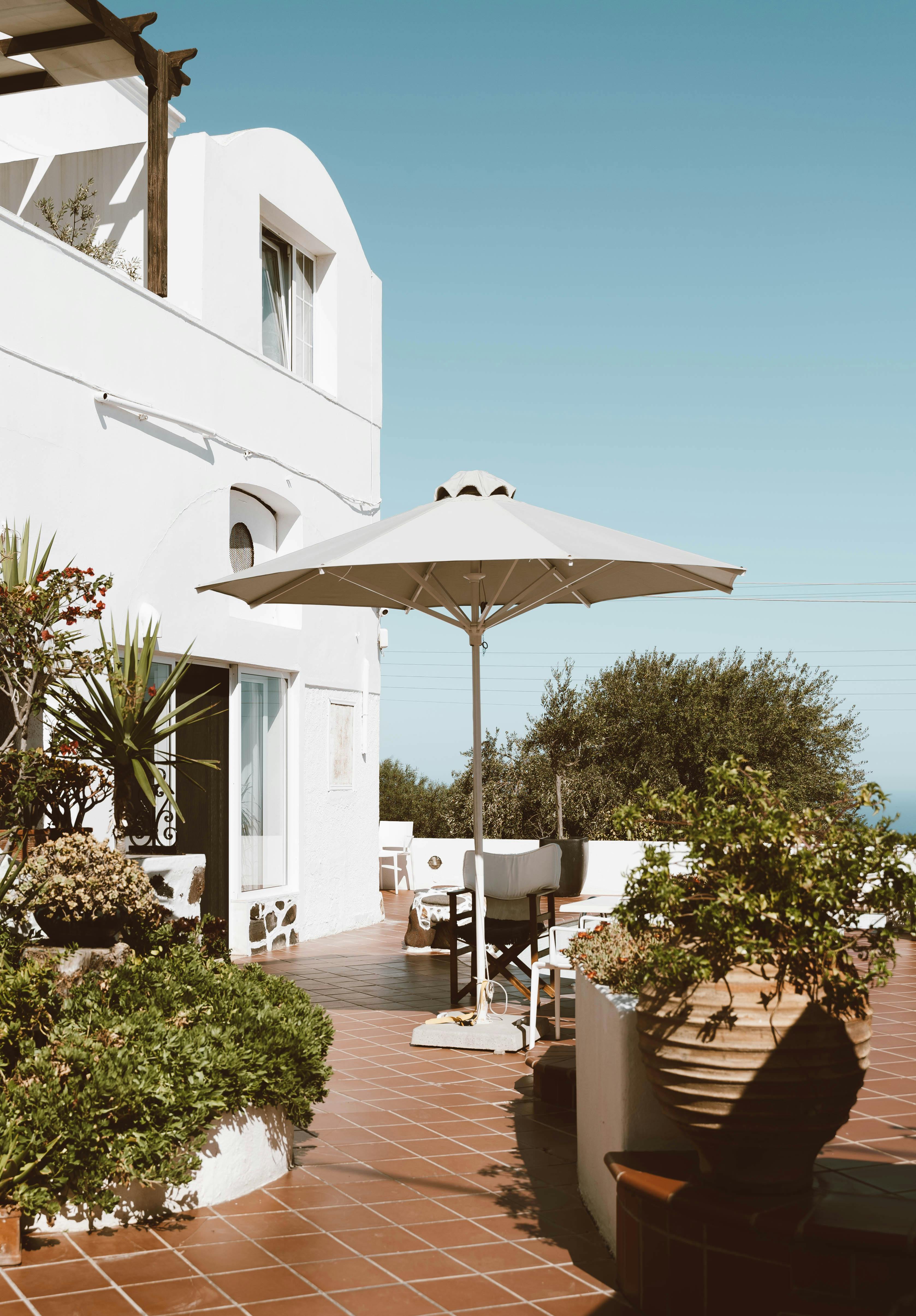 Peaceful outdoor terrace in Santorini with umbrella and lush greenery. Ideal vacation spot.