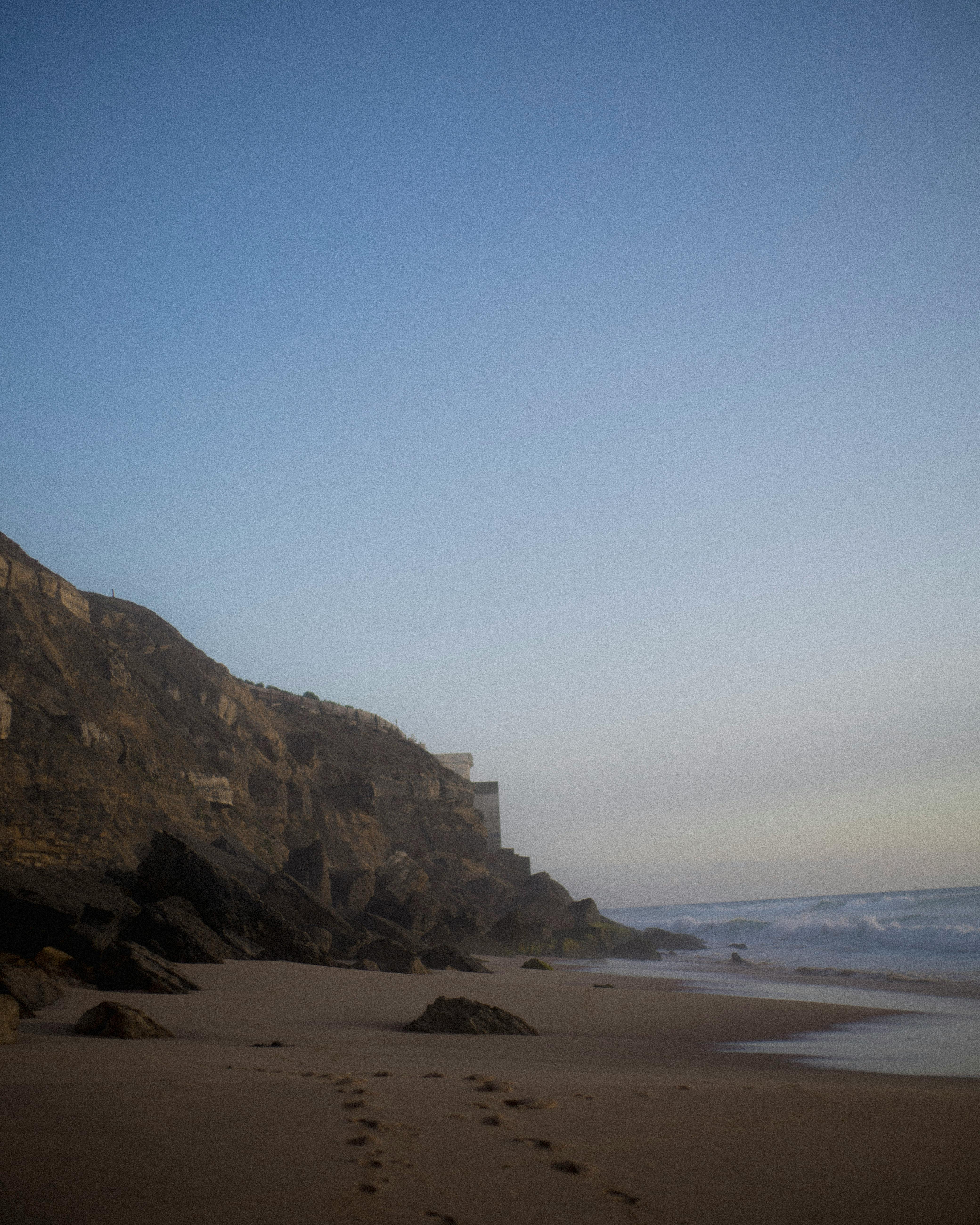 Tranquil beach scene with rocky cliffs and soft waves under a calming dusk sky.