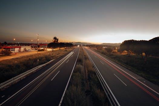 A serene expressway scene captured at sunset, with long exposure light trails and a golden horizon.