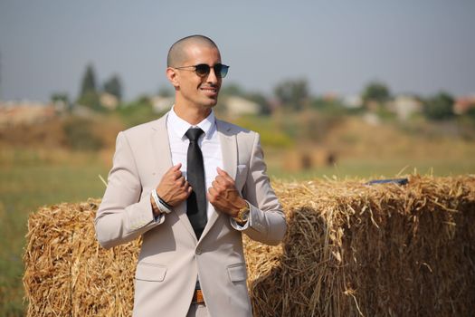 A man in a suit and tie standing in front of hay bales