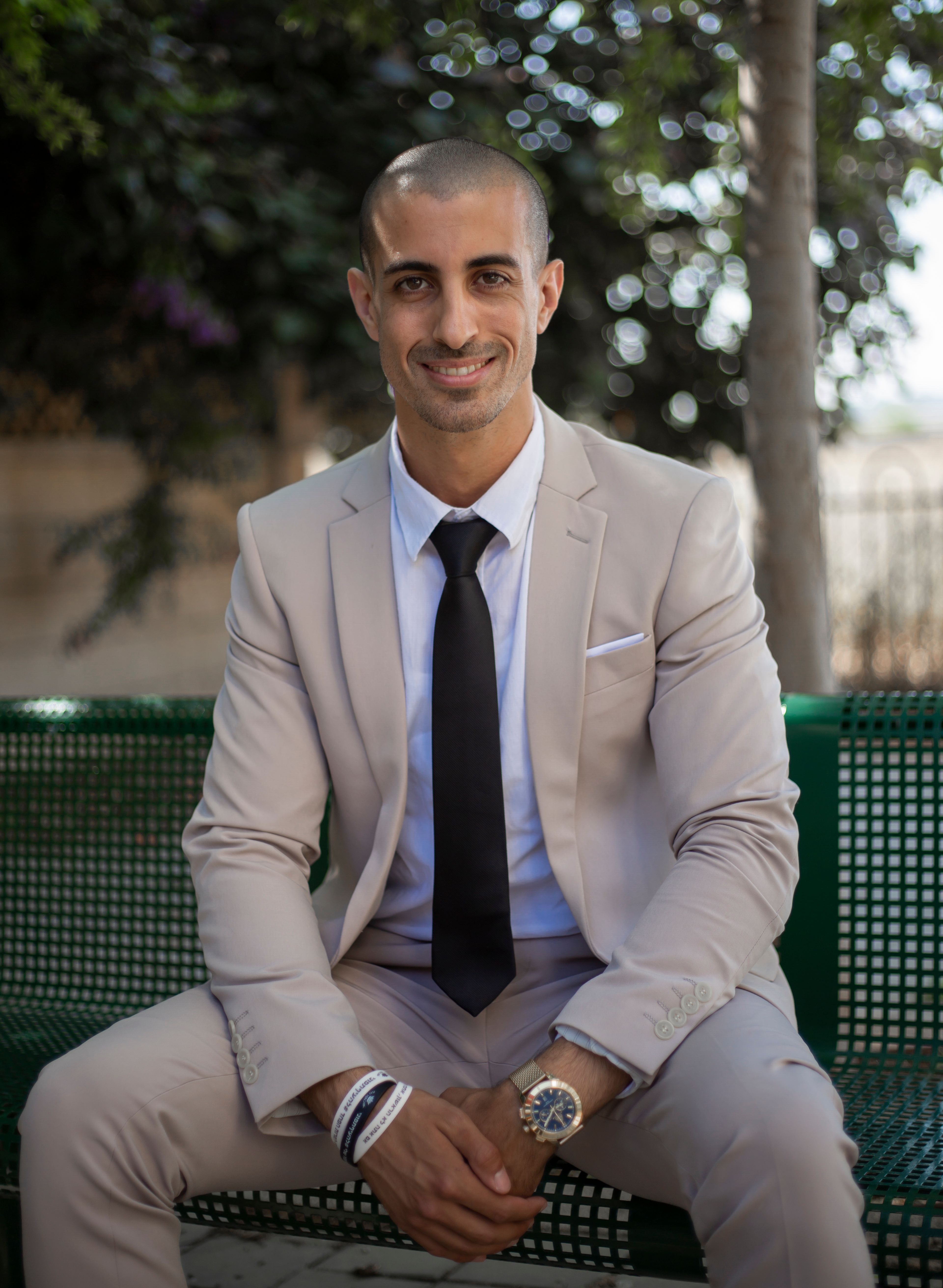 Professional businessman in a beige suit sitting on a bench outdoors, exuding confidence.