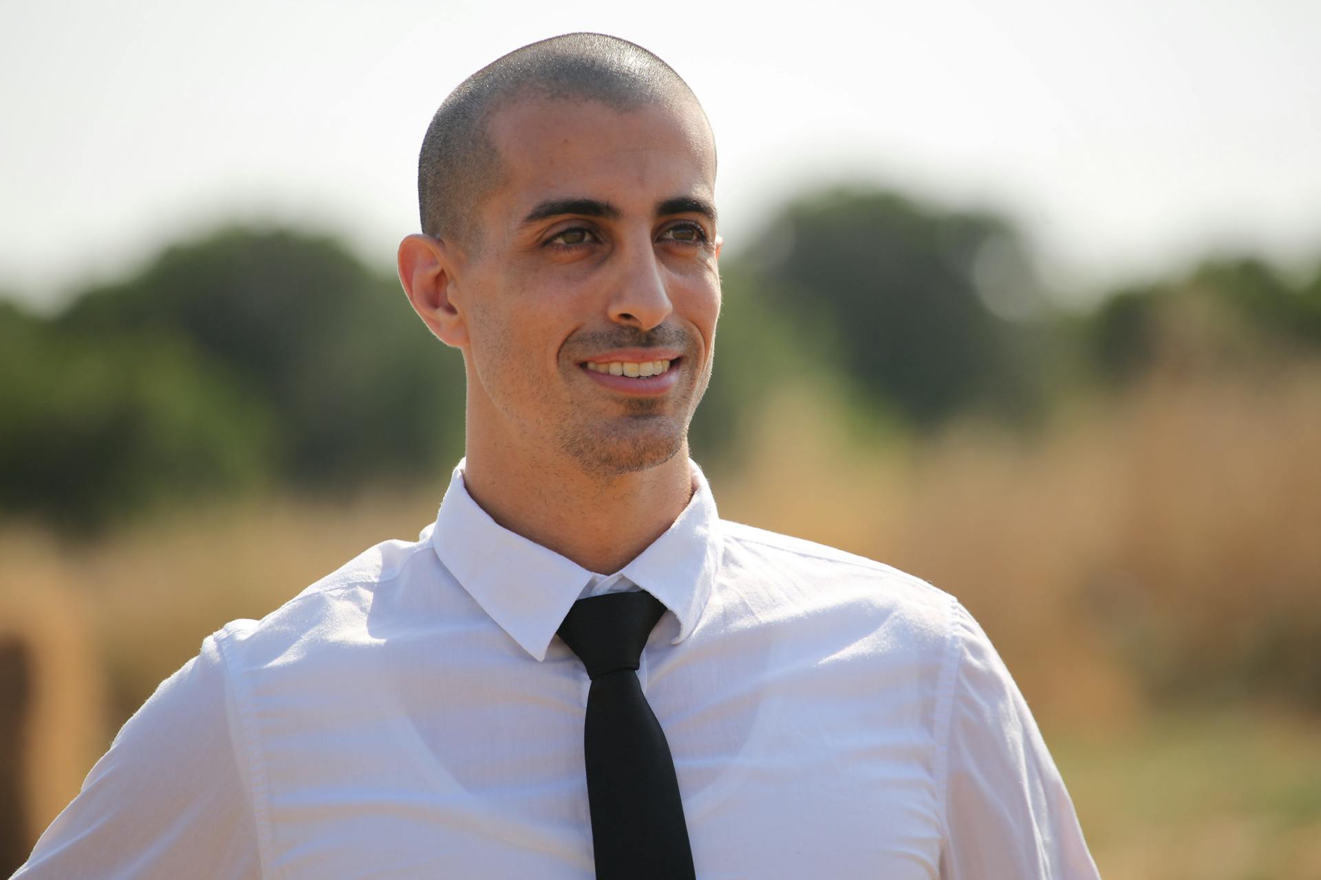 Portrait of a confident businessman smiling in an outdoor setting wearing a white shirt and tie.