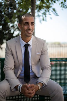 Smiling businessman sitting outdoors in a beige suit during daytime.