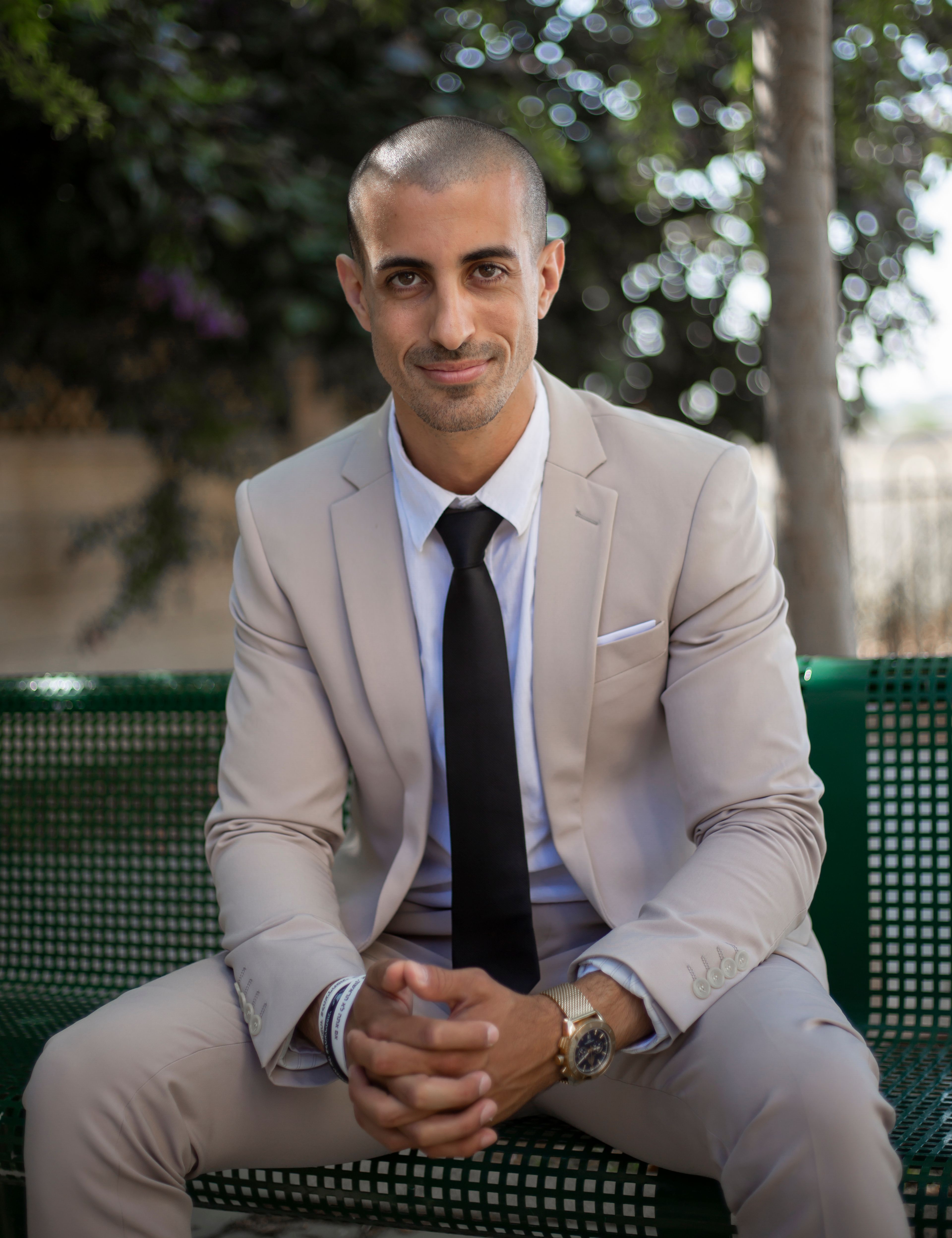 Young businessman in a beige suit sitting on a bench outside, exuding confidence.