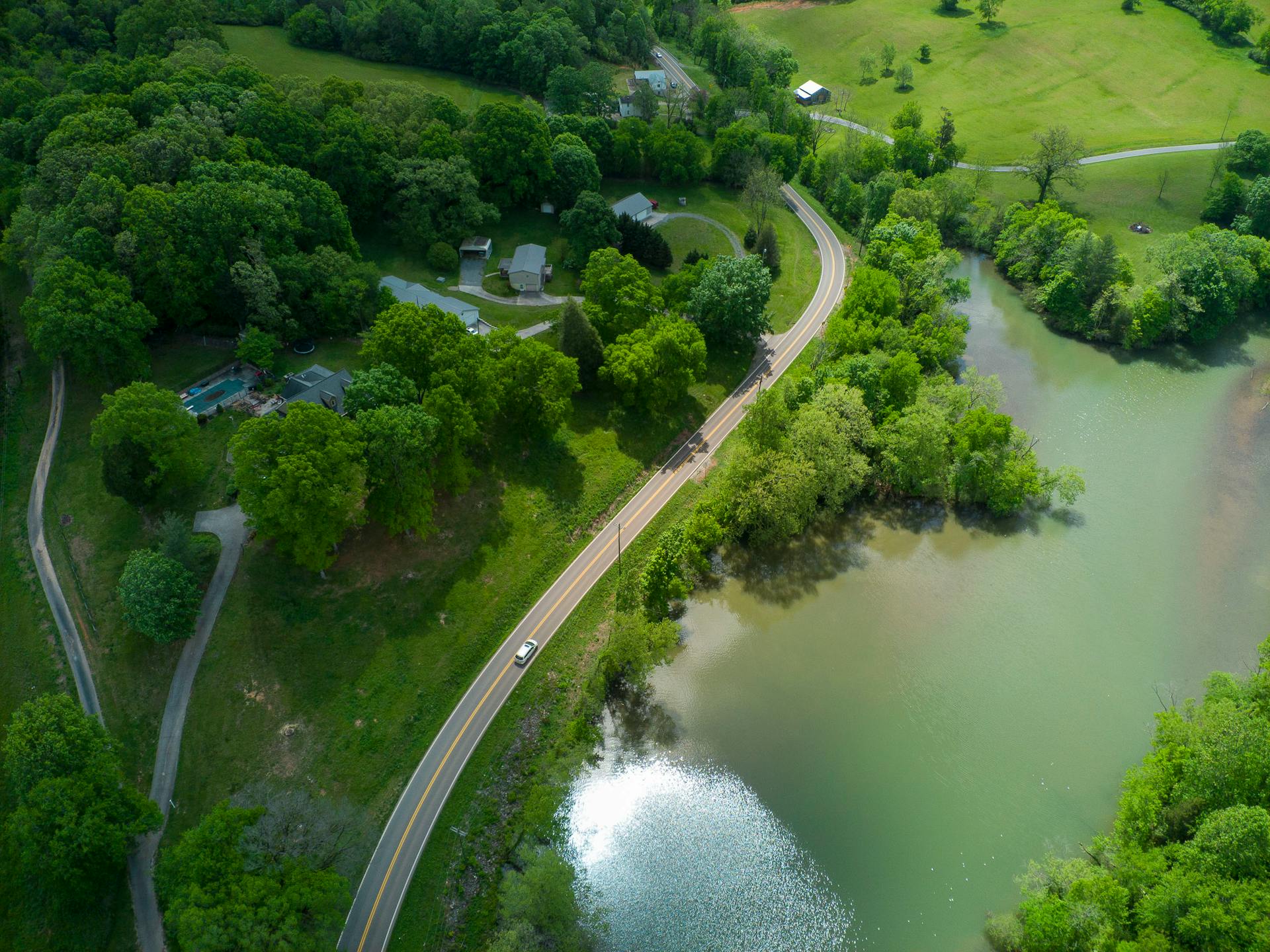 Stunning aerial photo of a countryside road winding by a lake in Loudon, TN. Lush greenery surrounds the landscape.