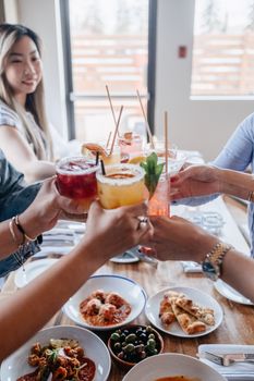 A group of adults enjoying drinks at a lively lunch, showcasing colorful cocktails and delicious meals.
