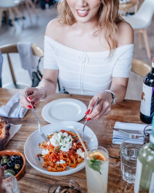 Free Elegant woman enjoying a meal in a modern restaurant setting, focusing on Italian pasta dish. Stock Photo