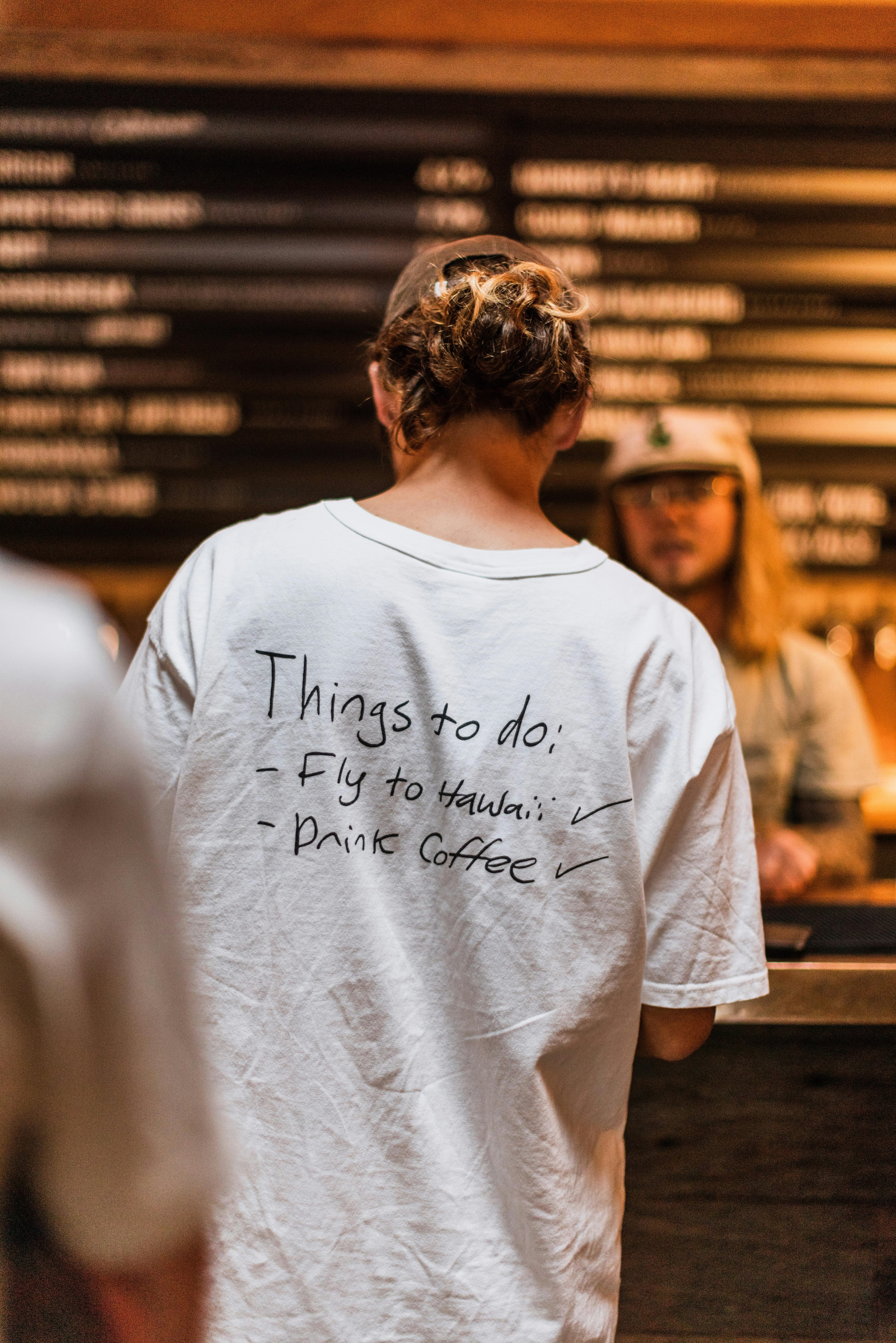 A person with a humorous t-shirt standing at a coffee shop counter, adding charm and relatability.