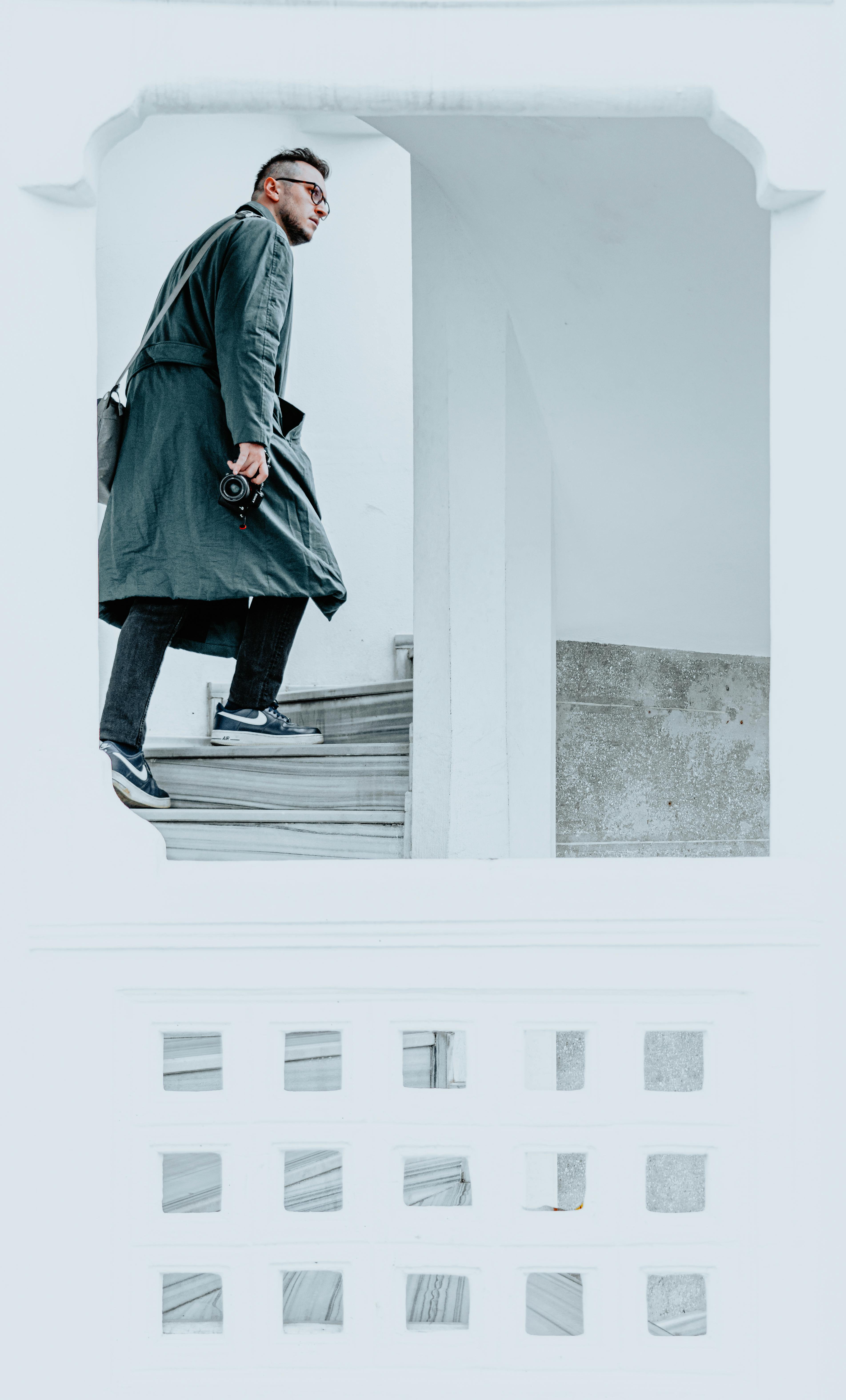 Man in a coat walking up a white staircase, capturing a modern urban vibe.