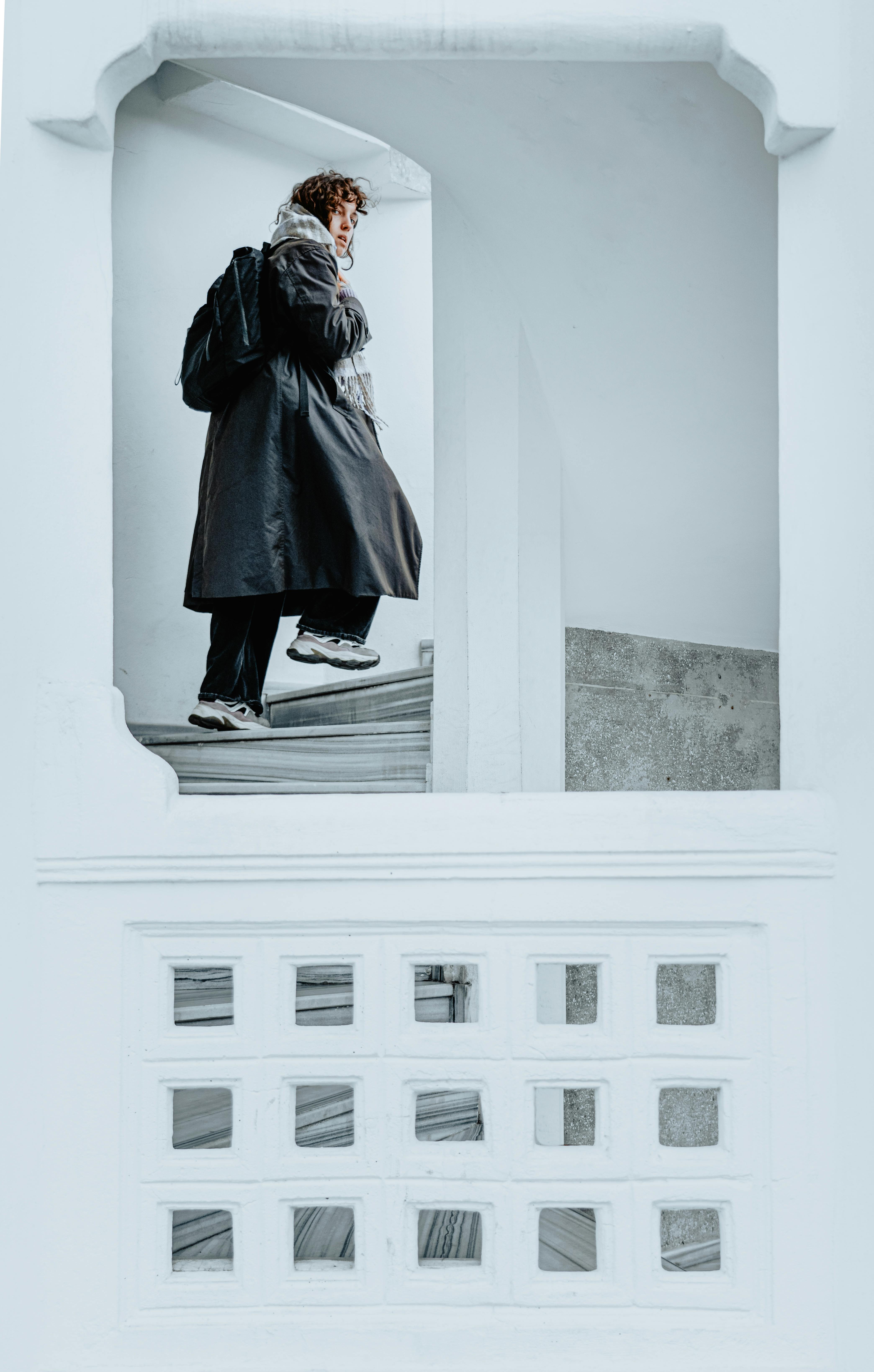 A person in winter attire walks up a stylish white staircase indoors.