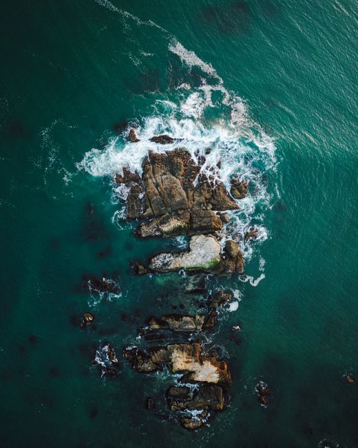 Stunning aerial view of ocean waves crashing over rugged rocks, creating dramatic seaside landscape.
