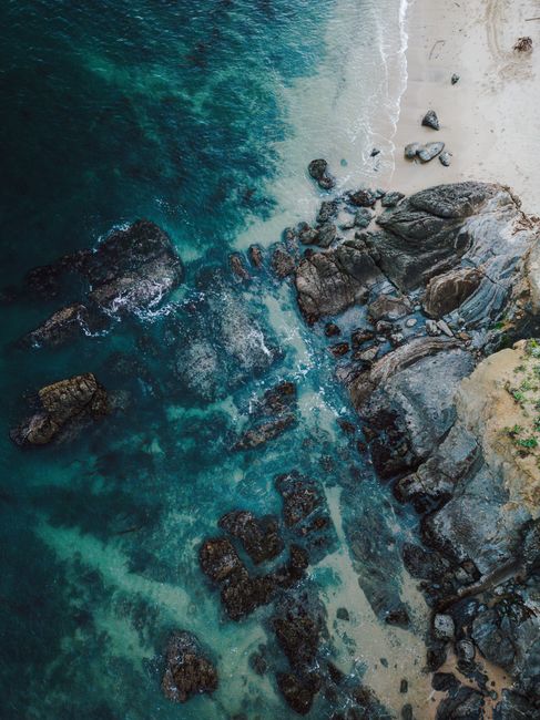 Stunning drone shot of a rocky shoreline with clear aqua waters and sandy beach.