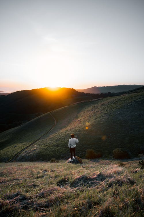Man Standing on Grassland on Hills at Sunset