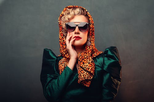 Fashionable woman posing with sunglasses and leopard print headscarf in a dramatic portrait.