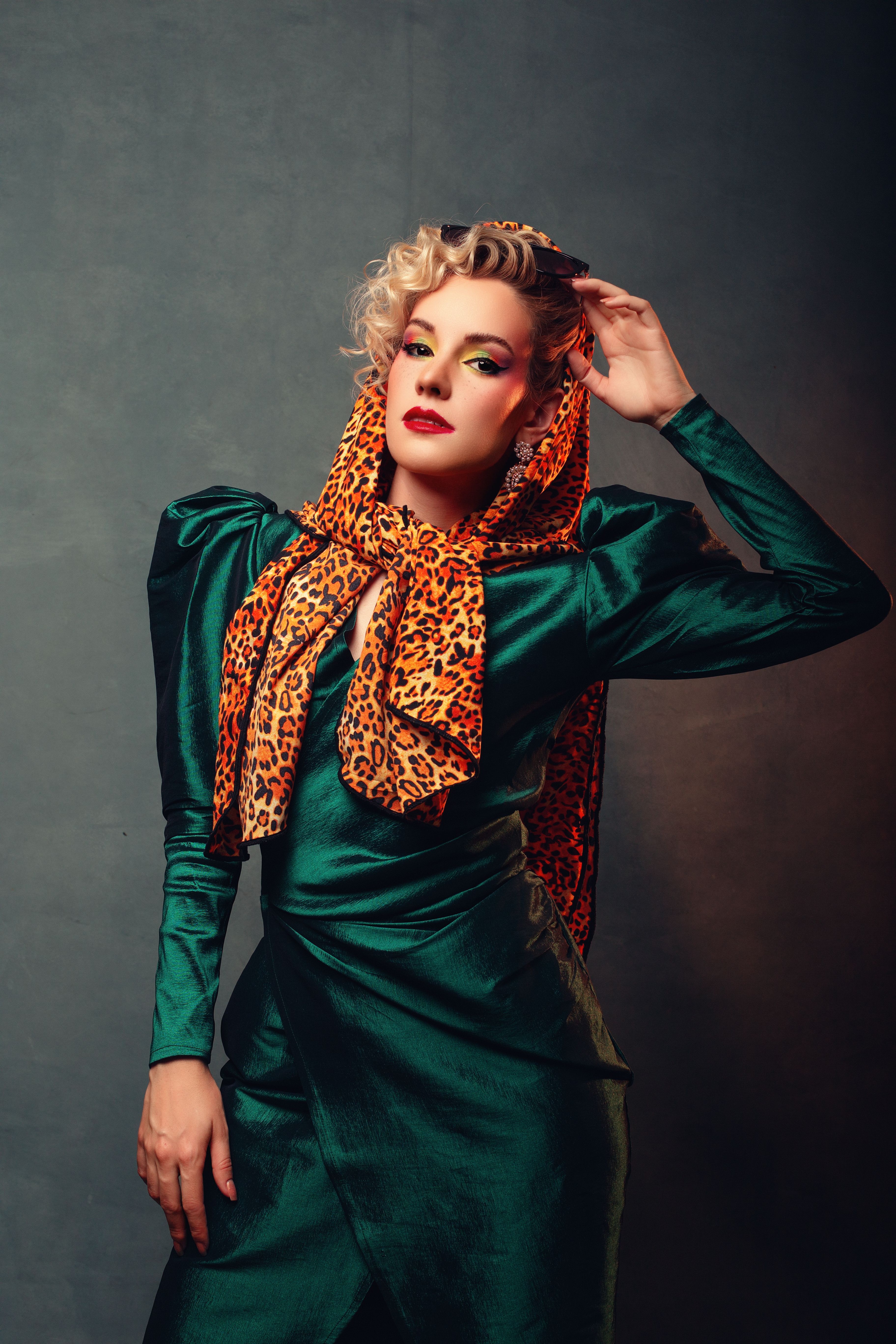 Stylish woman in green dress and leopard print shawl posing dramatically against a gray background.