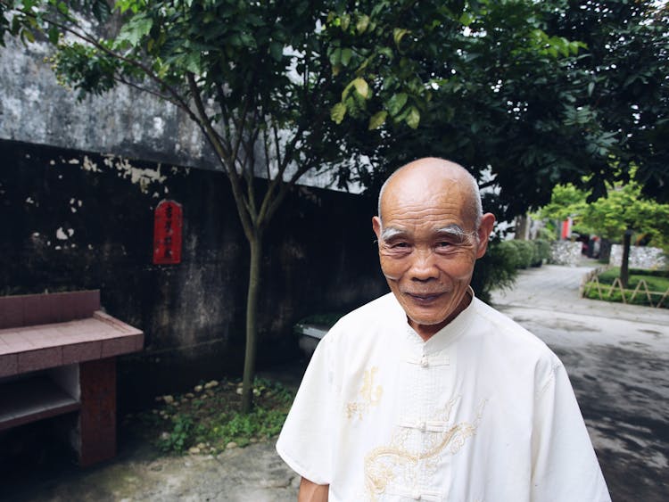 Portrait Of A Senior Man Wearing A White Shirt Standing In A Garden