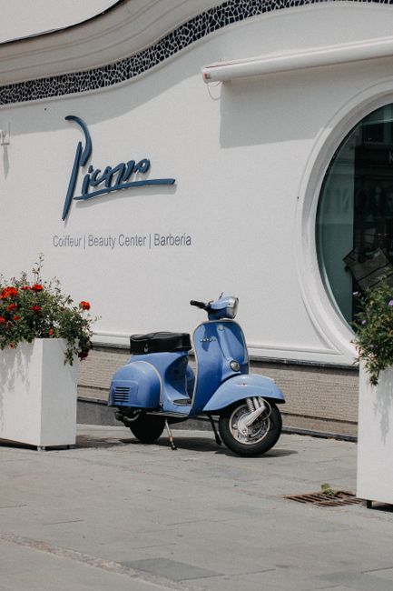 A classic blue scooter parked outside a beauty center on a sunny day.