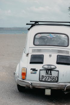 Classic white vintage car with license plate on sandy beach, rear view.
