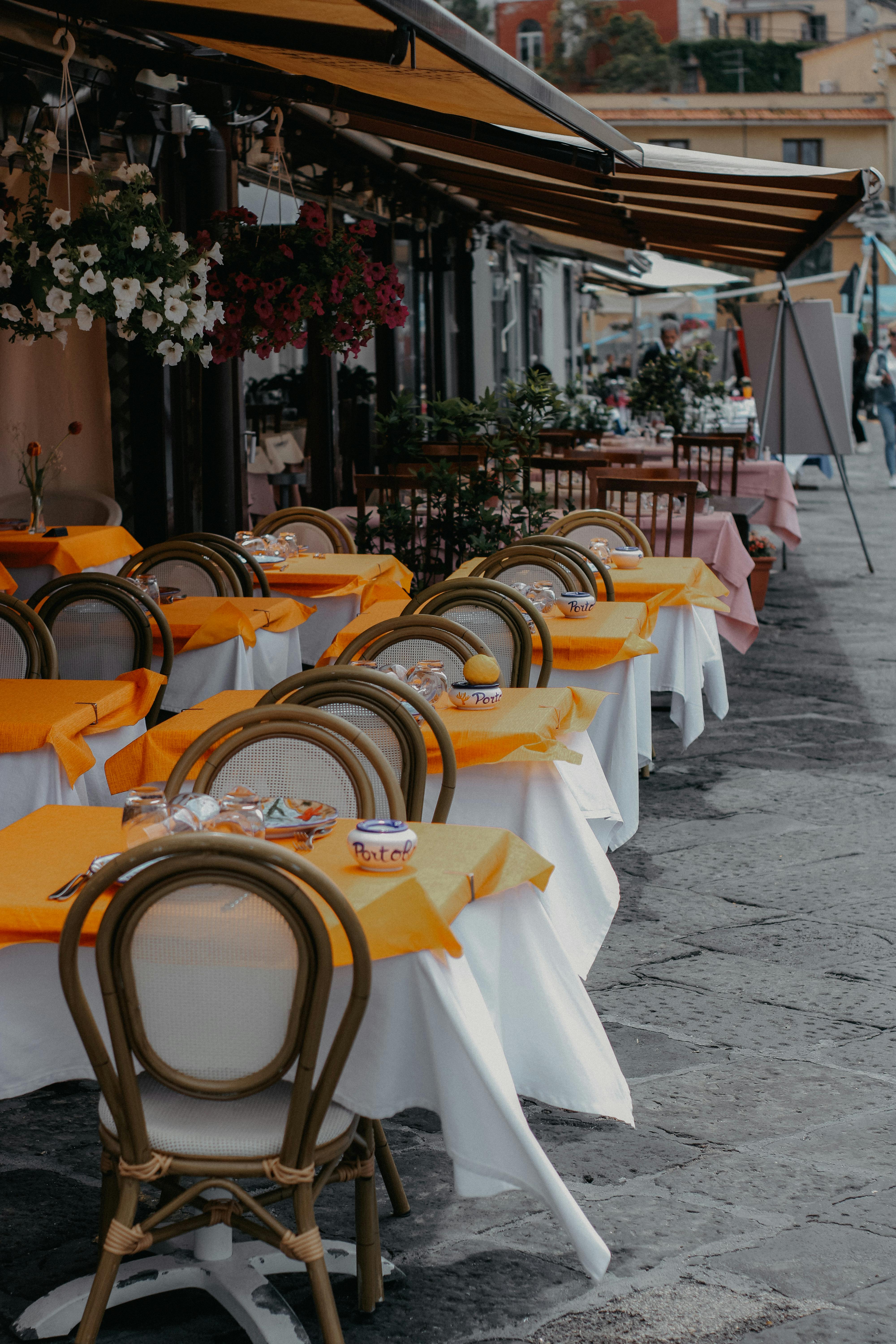 An inviting outdoor cafe with vibrant orange tablecloths and elegant chairs lined along a city street.