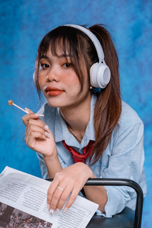 Portrait of a Young Woman Wearing Headphones Holding a Lollipop and a Newspaper