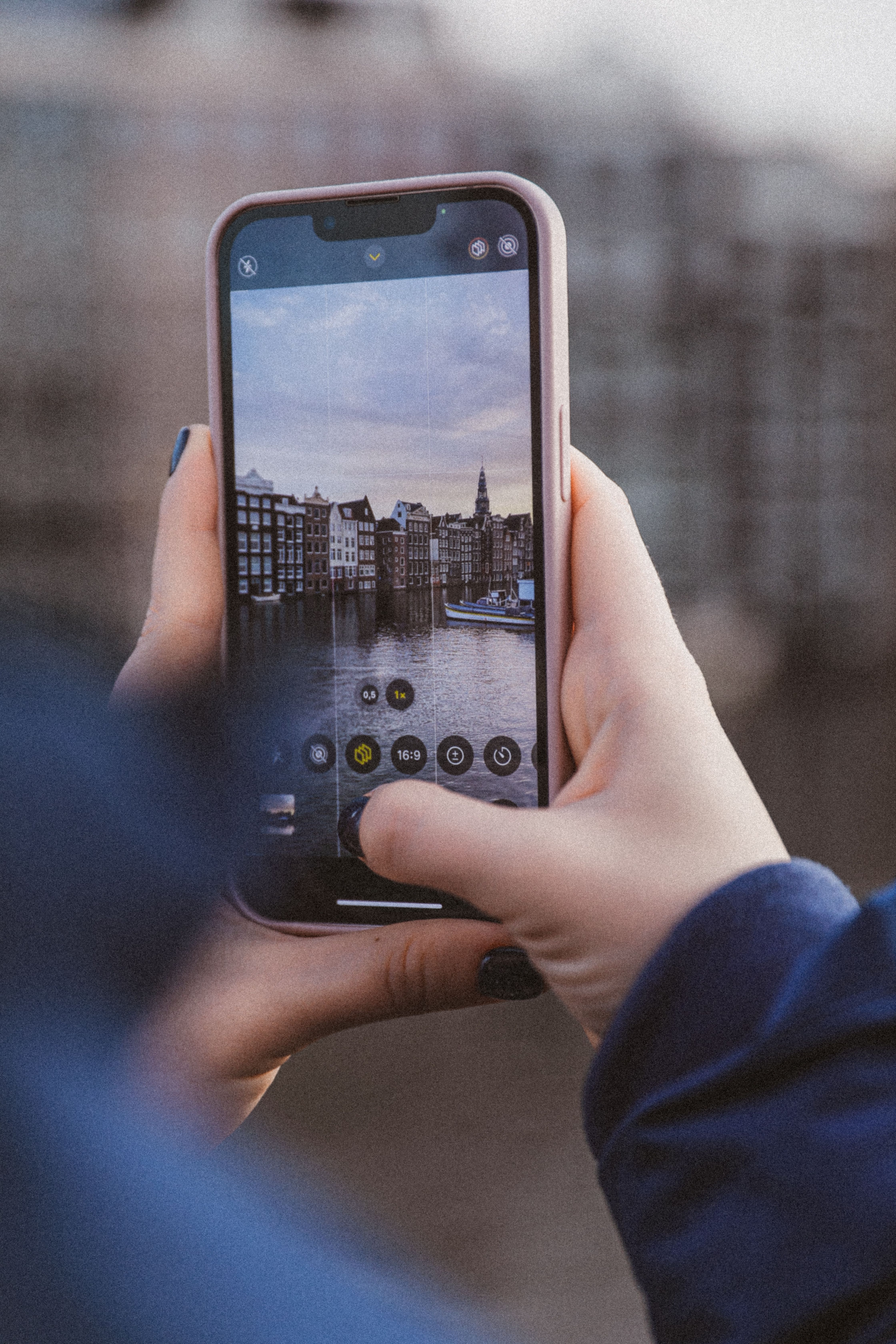 Hands holding smartphone taking photo of a cityscape with reflections.