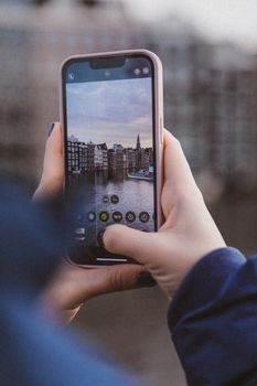 Hands holding smartphone taking photo of a cityscape with reflections.