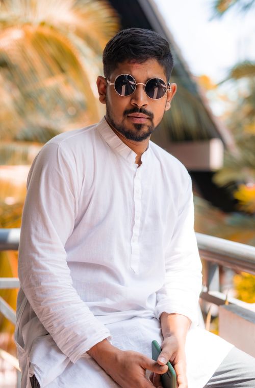 Free Portrait of a stylish man in sunglasses wearing a white shirt, seated outdoors. Stock Photo