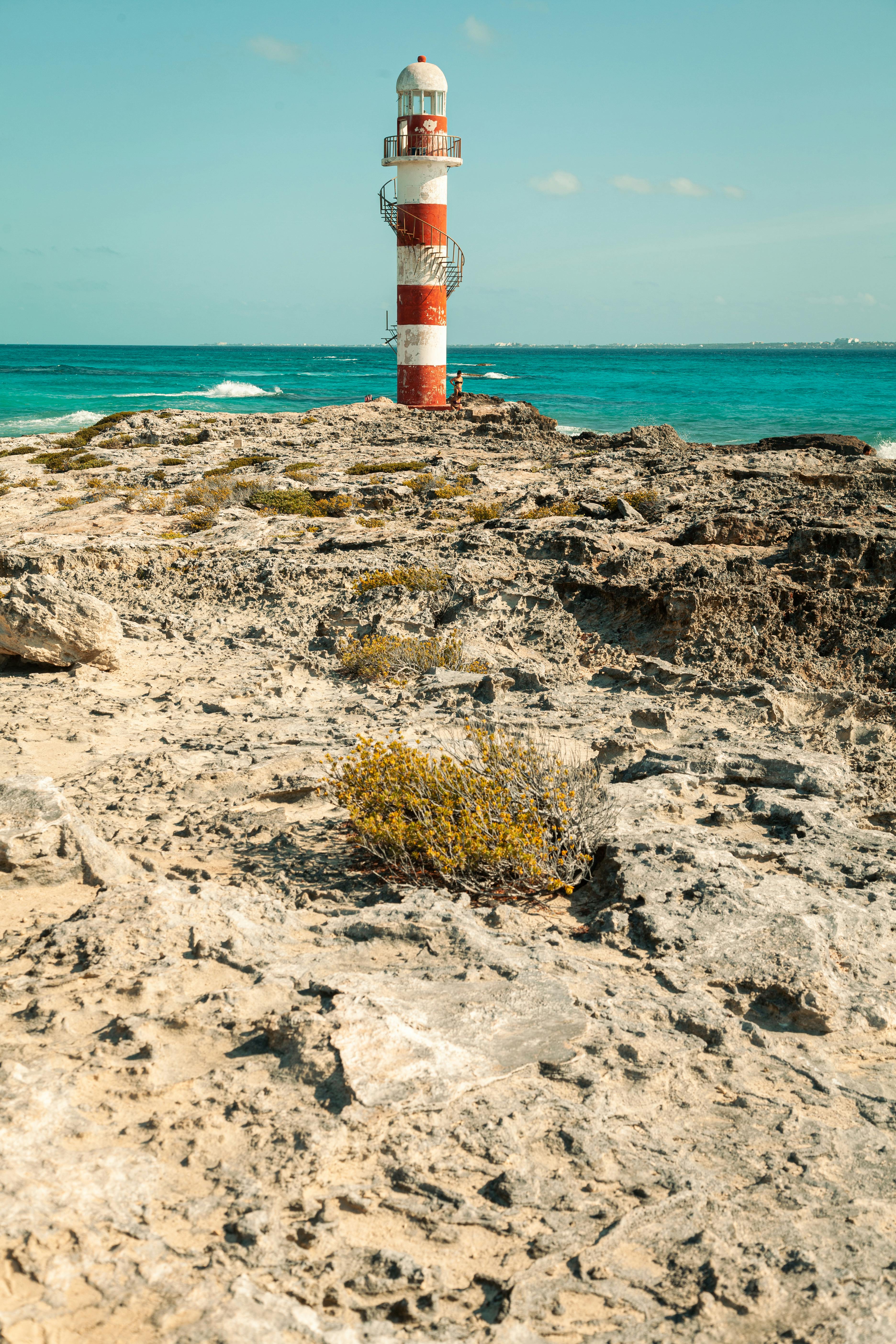 A picturesque view of the Punta Cancun Lighthouse on a rocky coastline with the turquoise sea in the background.